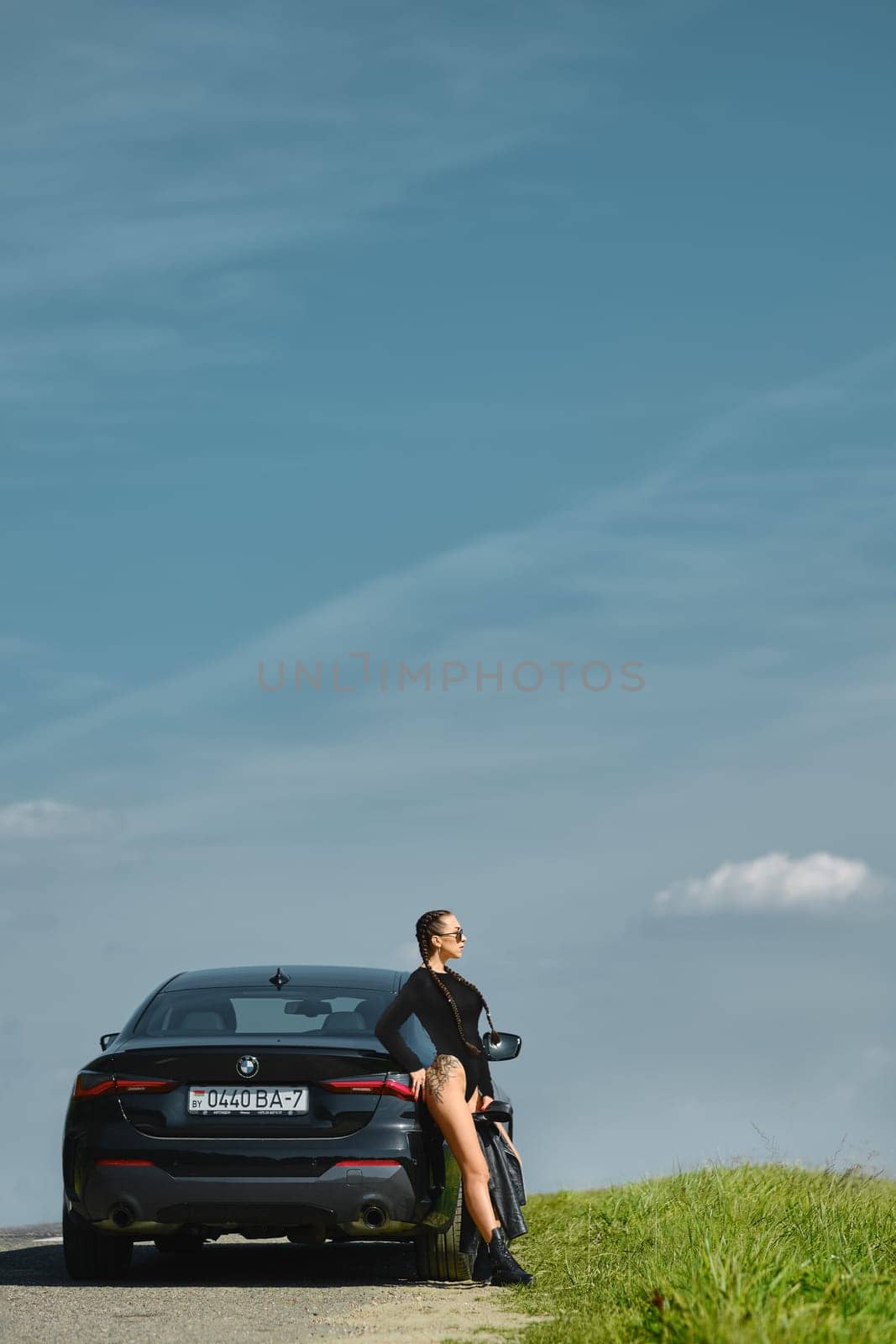 September 12, 2021, Minsk, Belarus - Beautiful young woman with tattoo on her hip and pigtails leaning to the car