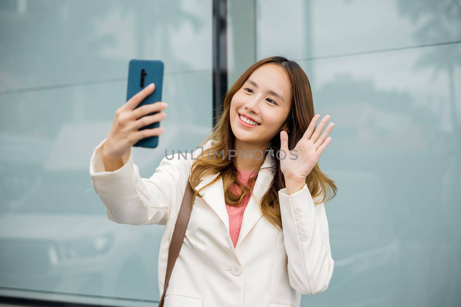 Happy business woman enjoying sunlight outdoors. Lifestyle and technology. Young Asian businesswoman during talking video chat in smart mobile phone outside in the city next the building