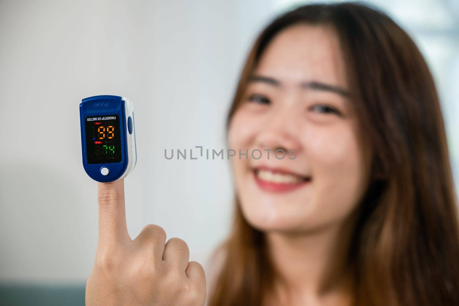 Asian young woman using medical oximeter equipment to measure pulse oxygen saturation on sofa in living room at home, Self healthcare with corona virus pandemic, medical healthcare