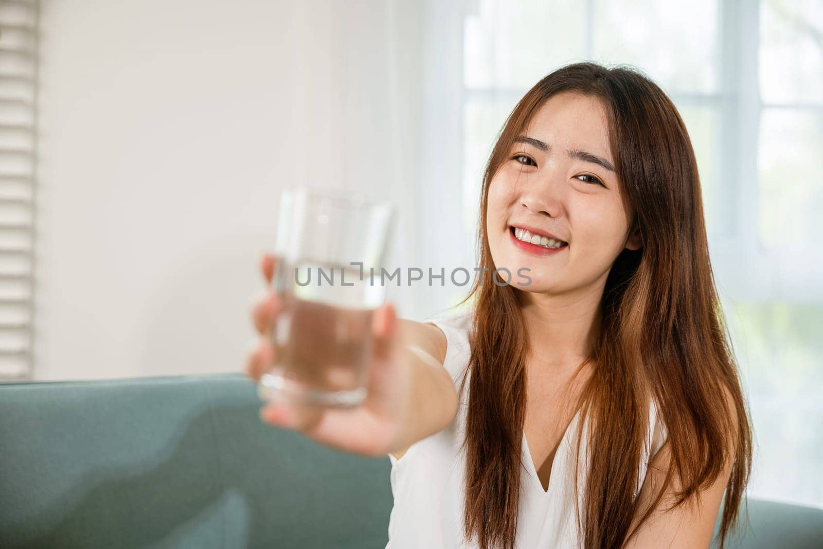 Happy smiling female beauty with water glass for drink in living room, Portrait of Asian young woman holding drinking nature water on hand at home, Healthy lifestyle