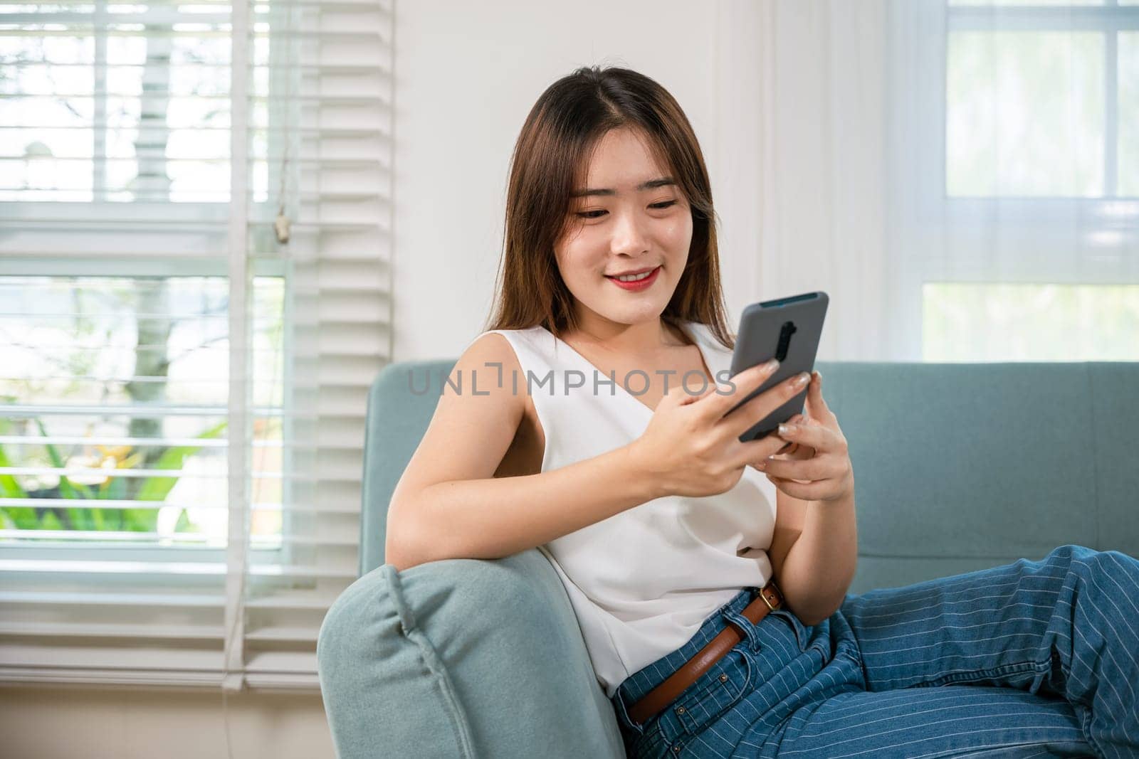 Happy beautiful woman relaxation she shopping online with smartphone, Smiling Asian female sitting on sofa talking mobile smart phone at living room at home, Social media networks communication