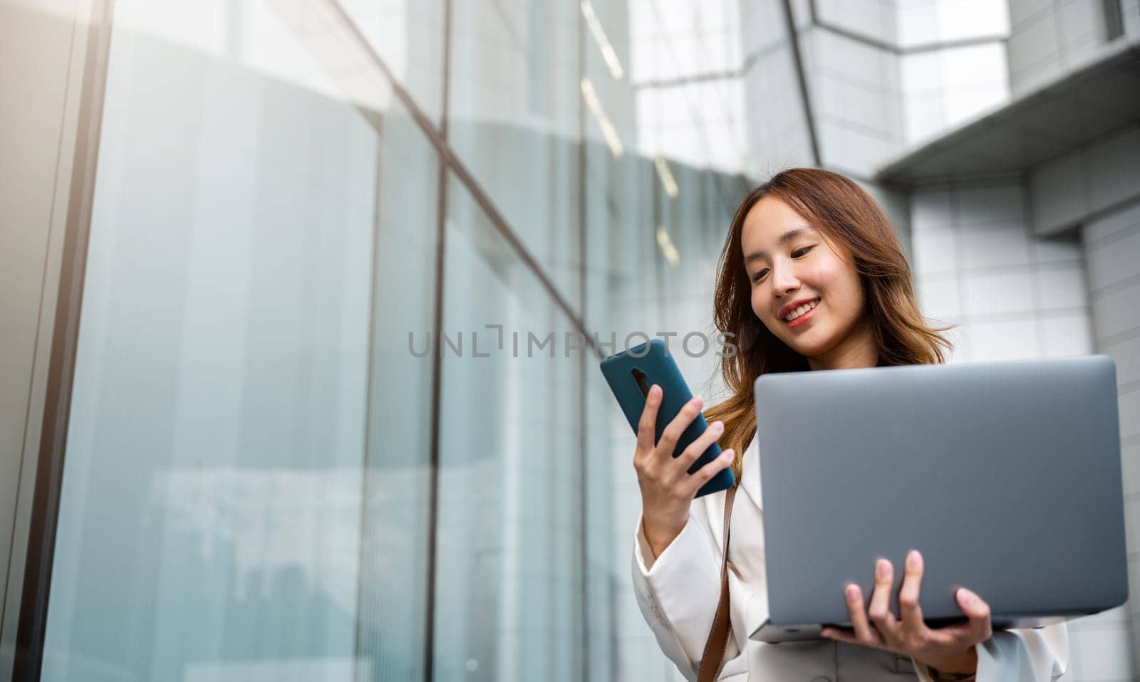 Confident businesswoman using smart phone with computer laptop standing in the city. Beautiful businesswoman being ready to work. Business concept.