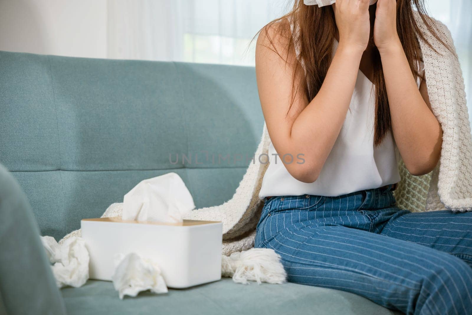 Sick female sitting under blanket on sofa and sneeze with tissue paper in living room, fever caught cold, Asian young woman she sick blowing nose sneezing in tissue at home, medicine healthcare