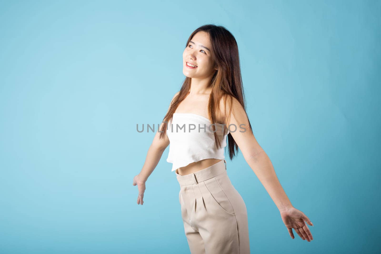 Happy woman smiling alone freedom carefree, Asian young female arms open to sunlight studio shot isolated on blue background welcome