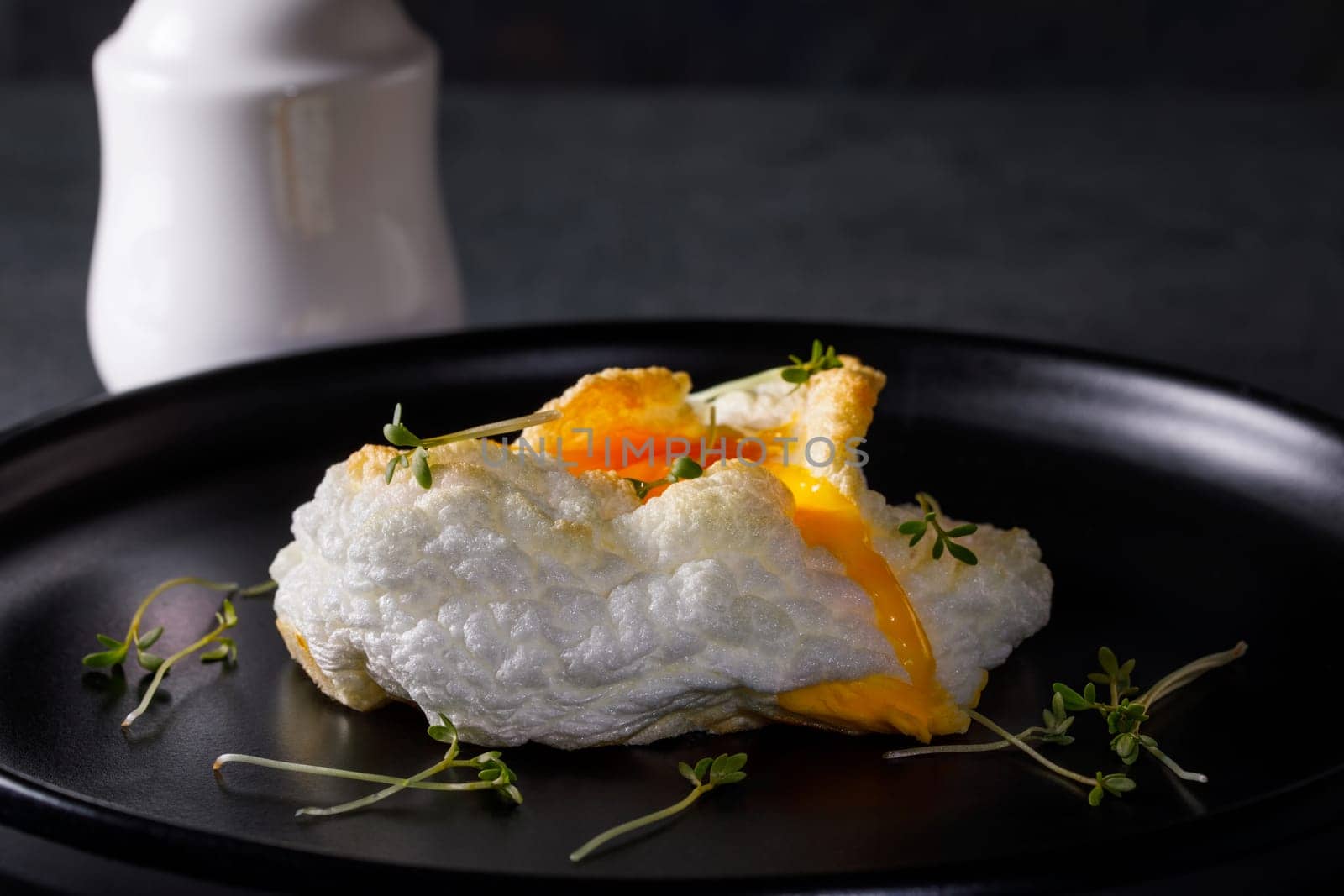 Tender baked egg. Orsini eggs in a cloud. French breakfast on a dark dish with a white salt shaker.