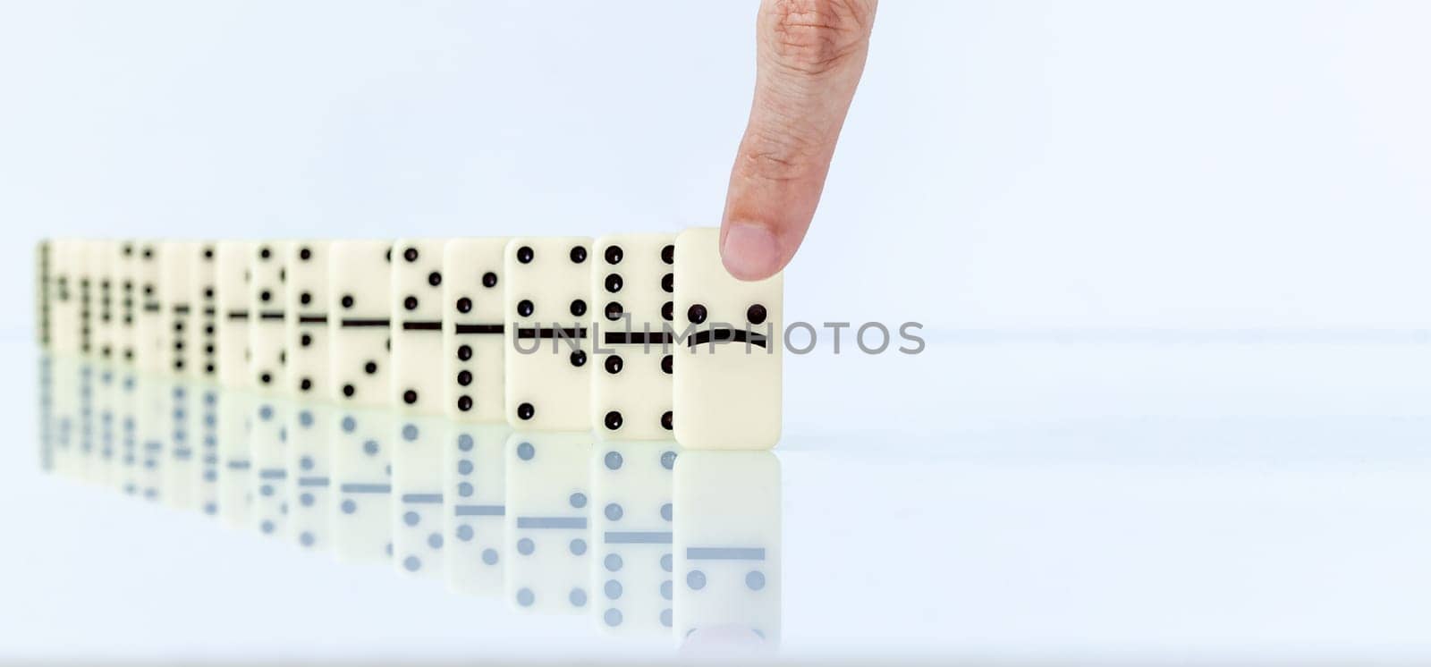Human finger starting domino effect falling on white background.