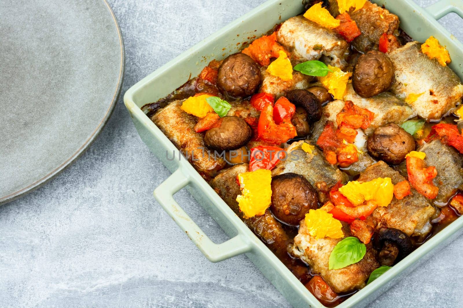 Diet fish hake cooked with mushrooms, orange and tomatoes. White fish in the oven dish