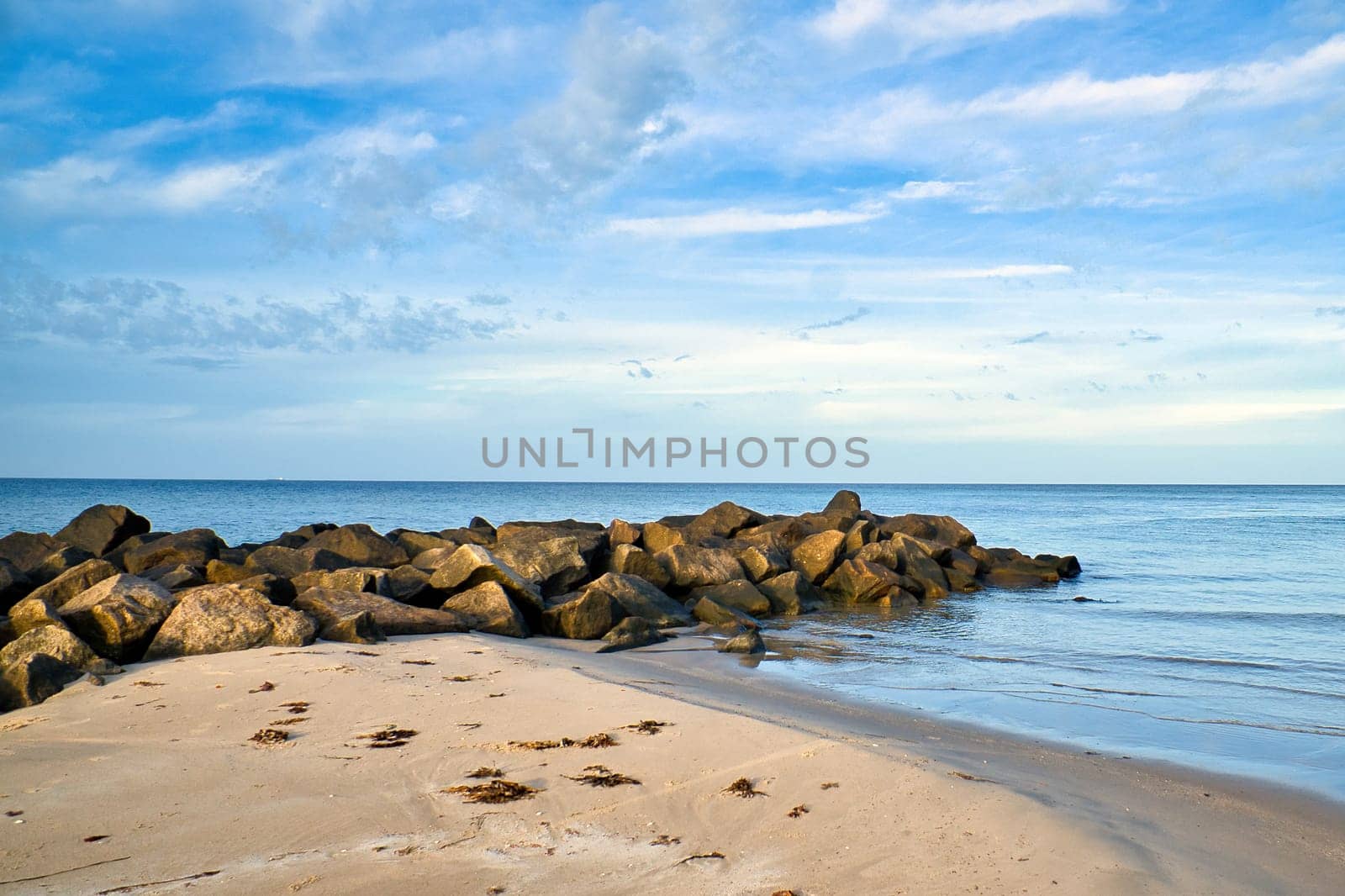 Stone groyne jutting into sea in Denmark with clouds in sky. Coastal landscape in Denmark. Landscape photo from ocean