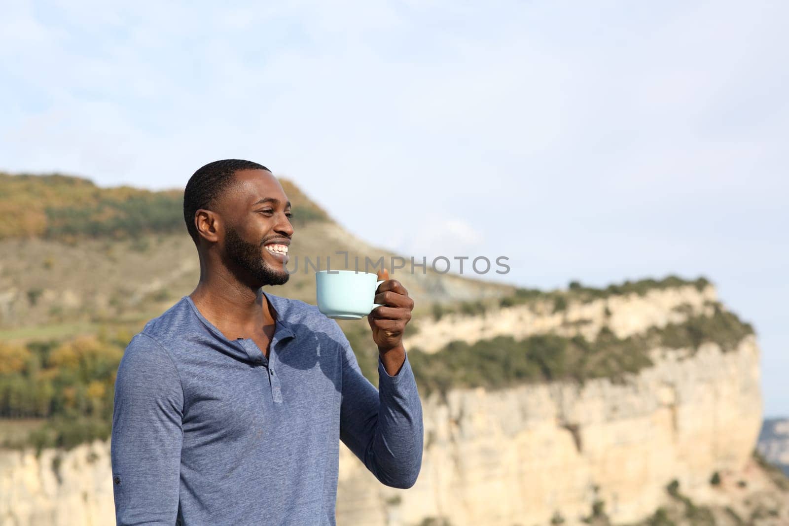 Happy black man drinking coffee contemplating views in the mountain