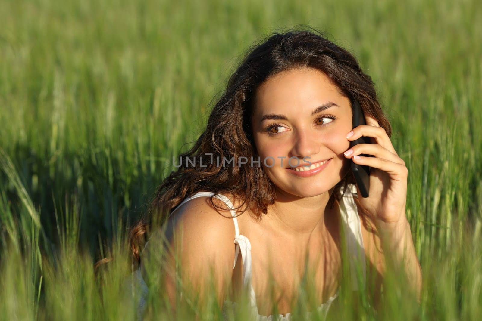 Happy woman talking on mobile phone in a green wheat field