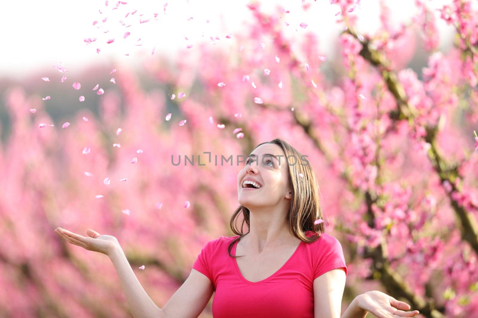 Happy woman throwing pink petals to the air in a field
