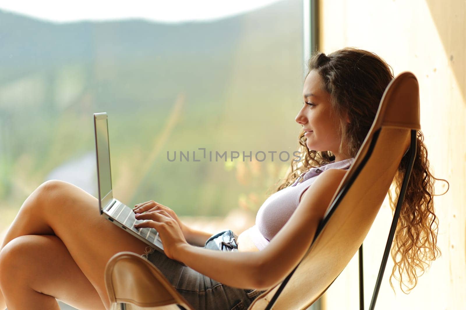 Side view portrait of a woman using laptop on a chair at home