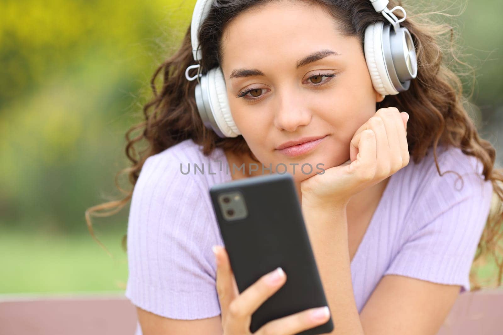 Woman listening to music with headphones in a park checking phone
