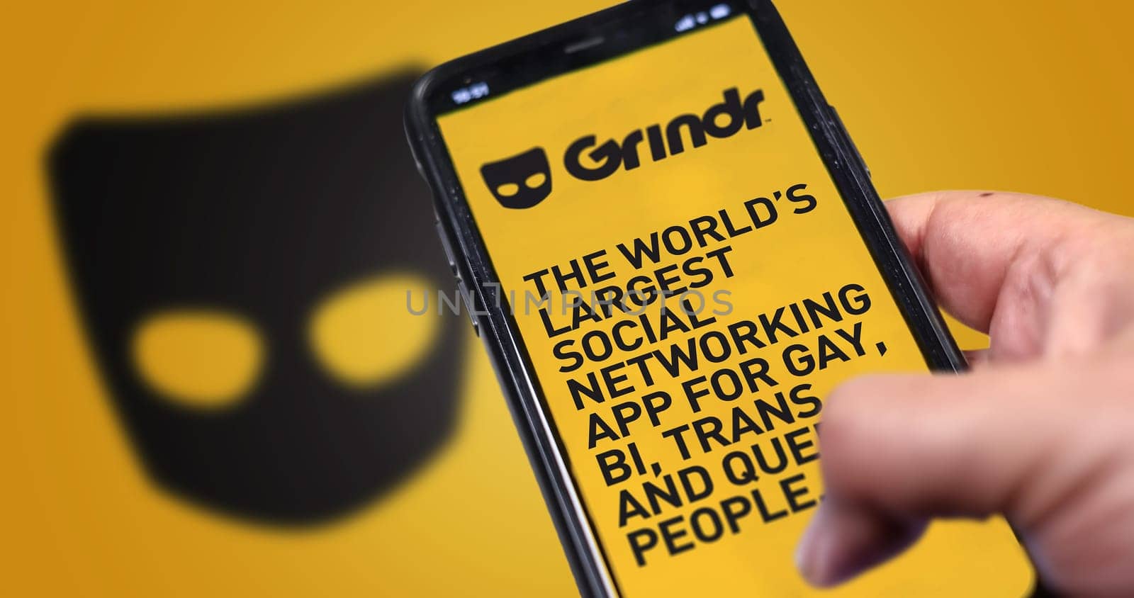 San Francisco, CA, US, May 2022: hand holding a phone with Grindr mobile application on screen. In background the Grindr logo blurred. Grindr is dating application for gay, bi, trans, and queer people