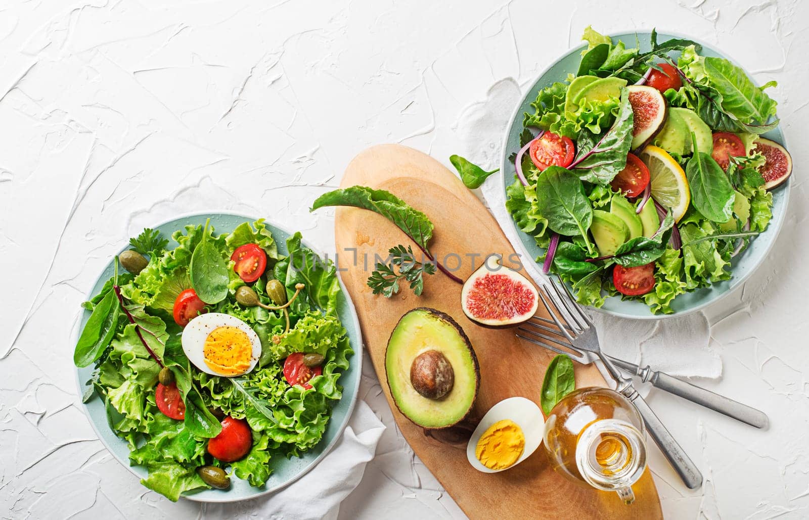 Fresh green lettuce salads with mixed vegetables, egg and fig on white table background