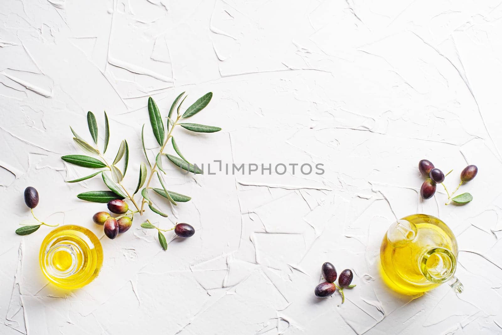 Olive oil in bowl with fresh olives fruit and olive branch on white background close up
