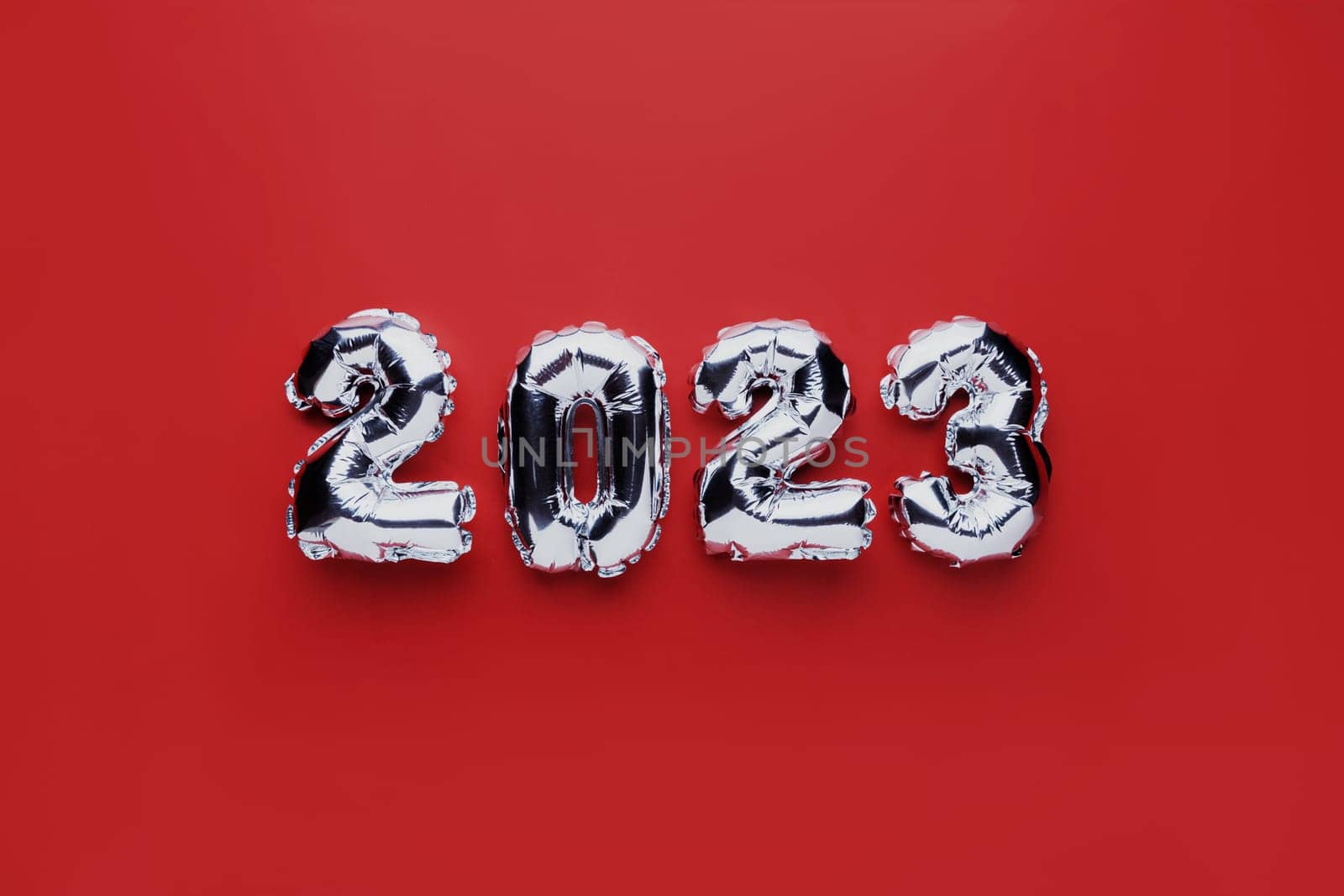 Christmas or New Year background. Red color flat lay with silver shiny 2023 balloon numbers in the center. Simple minimalistic greeting card.