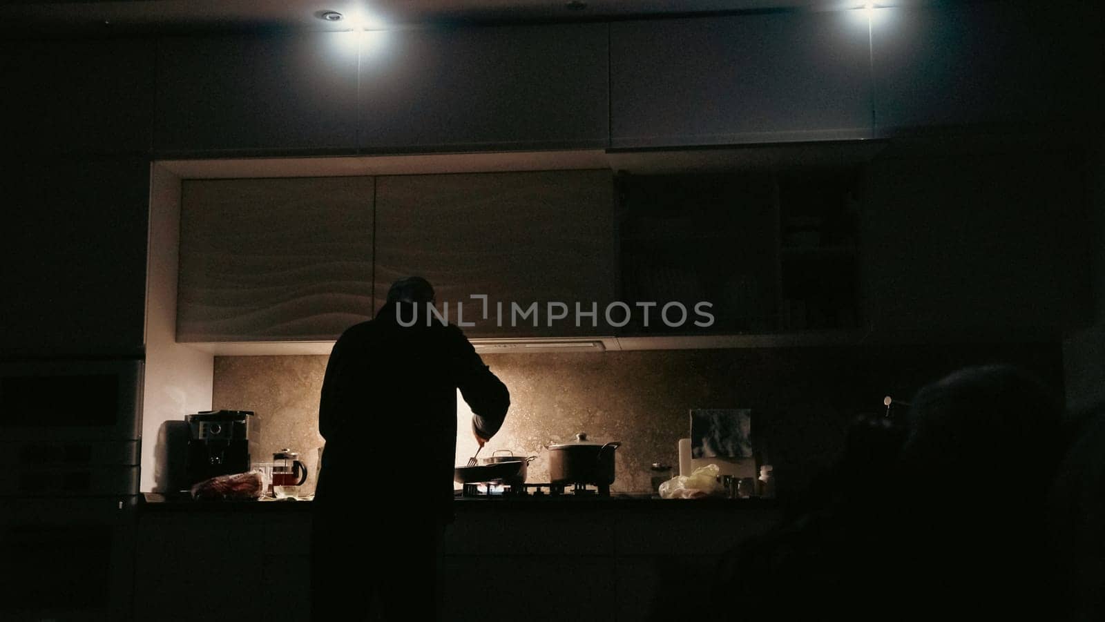 Man cooking with flashlights on a kitchen during blackout in ukraine. Blackout in Ukraine concept. Man cooking in a darkness with flashlights around.