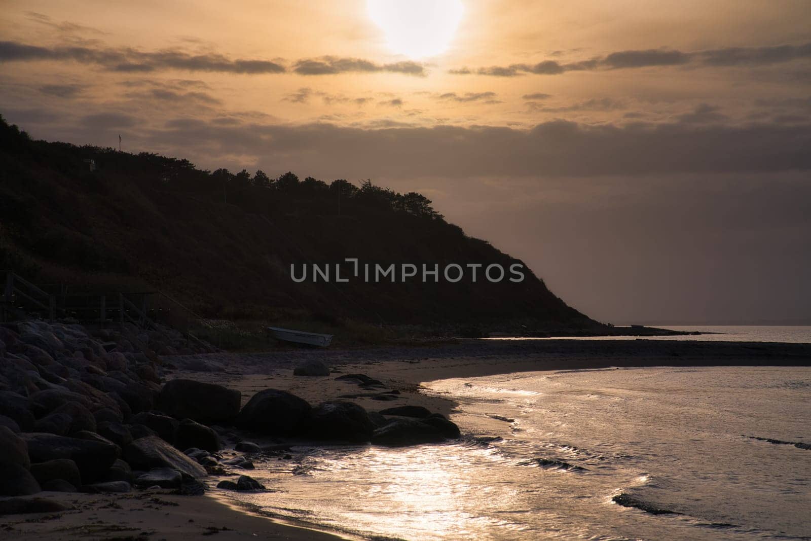 Sunset on the Danish coast. Beach, waves. Hill with trees in background. Landscape photo from sea