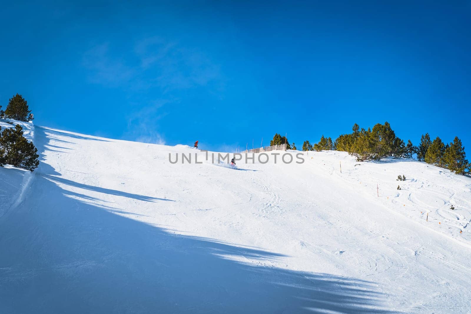 Couple of skiers having fun and going fast on steep piste or ski slope in Pyrenees Mountains. Winter ski holidays in El Tarter, Grandvalira, Andorra
