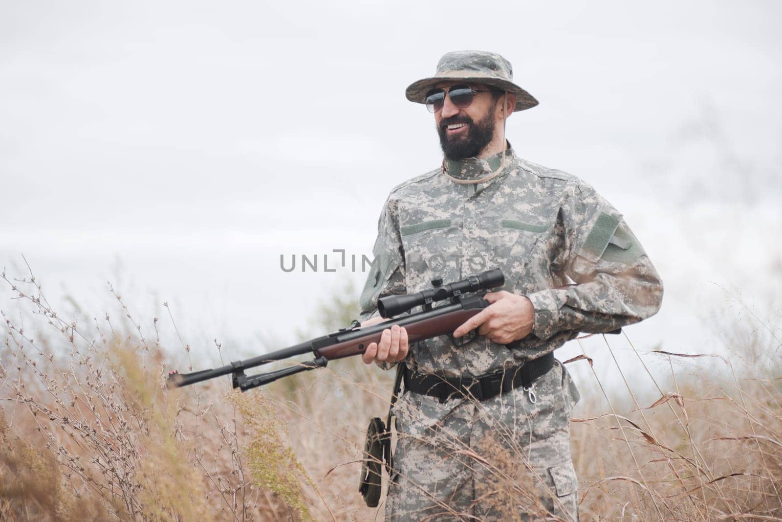 The smiling hunter or rifleman with shotgun or air gun is standing in nature.