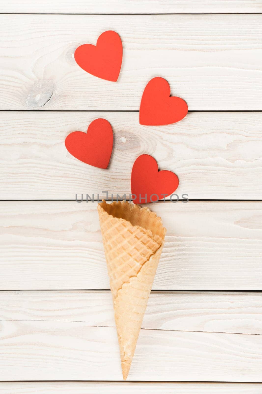 Vertical shot of hearts moving from waffle cone like confetti on light wooden background. Ice cream dessert and other sweets as present on saint Valentine's Day. Love and romance. Copy space, flat lay