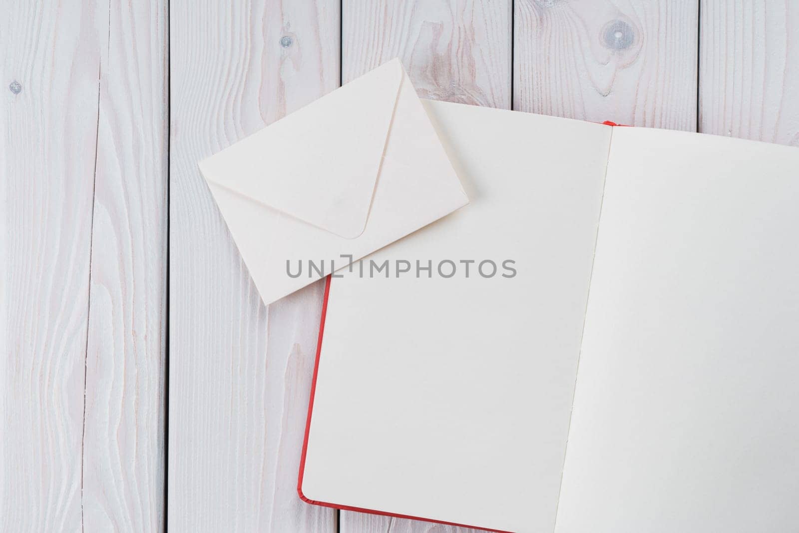 Red diary book with white paper with handmade, craft envelope on light wooden desk background. Traditional message letters sending, postal cards for business and lifestyle. Copy space, flat lay