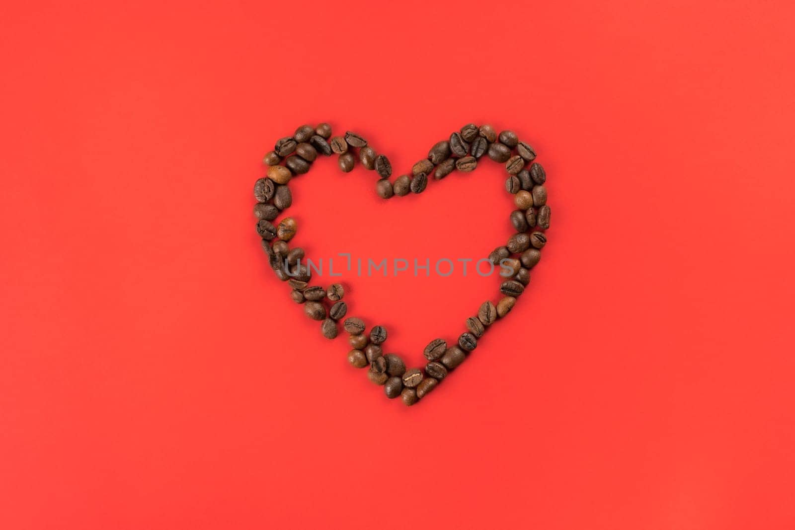 Brown coffee beans forming heart contour on red studio background. Charity and donation on holidays. Falling in love and confession on saint valentines day. I give you my heart. Flat lay, copy space