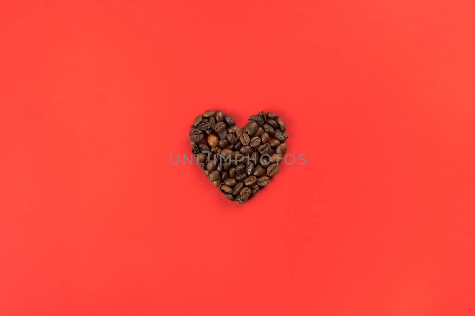 Coffee beans forming heart shape on red studio background. Charity and donation on holidays. I give you all my heart. Falling in love and confession on saint valentines day. Flat lay, copy space