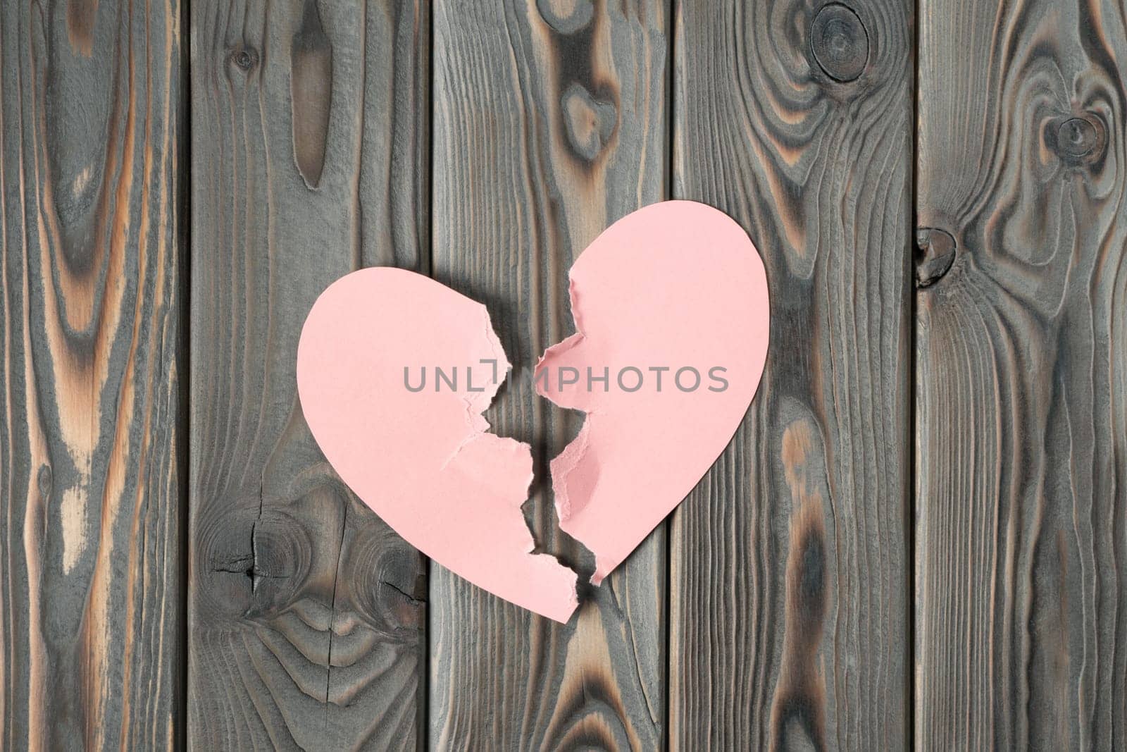 Pink torn paper heart halves laying together on dark wooden table. Broken heart, breaking up, past relationship and rejection on saint valentines day. Unspoken feelings. Top view, copy space, flat lay