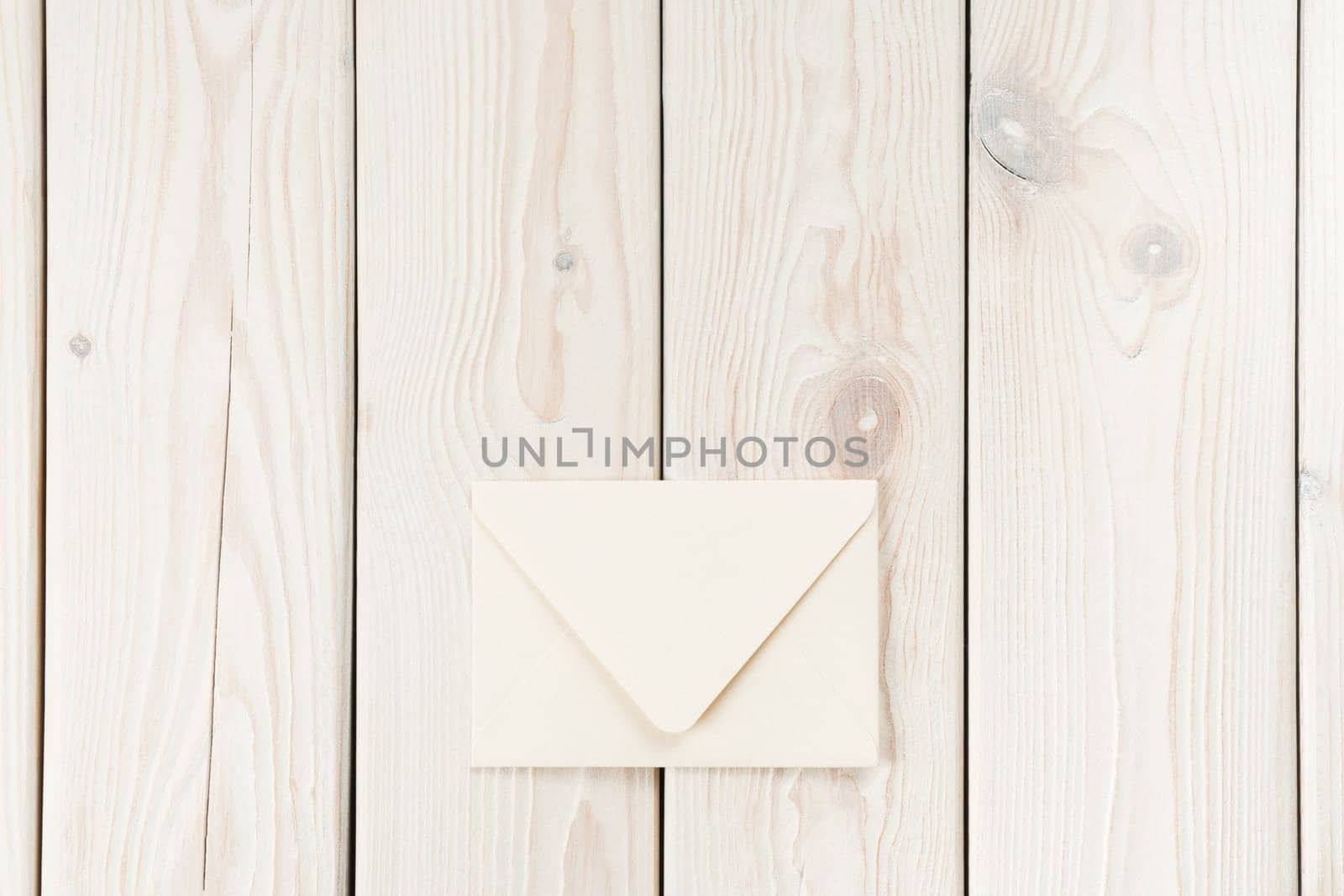 White craft handmade closed paper envelope laying on white wooden plank background. Post card message, letter sending. New delivery and retro traditional invitation. Copy space, mockup, flat lay