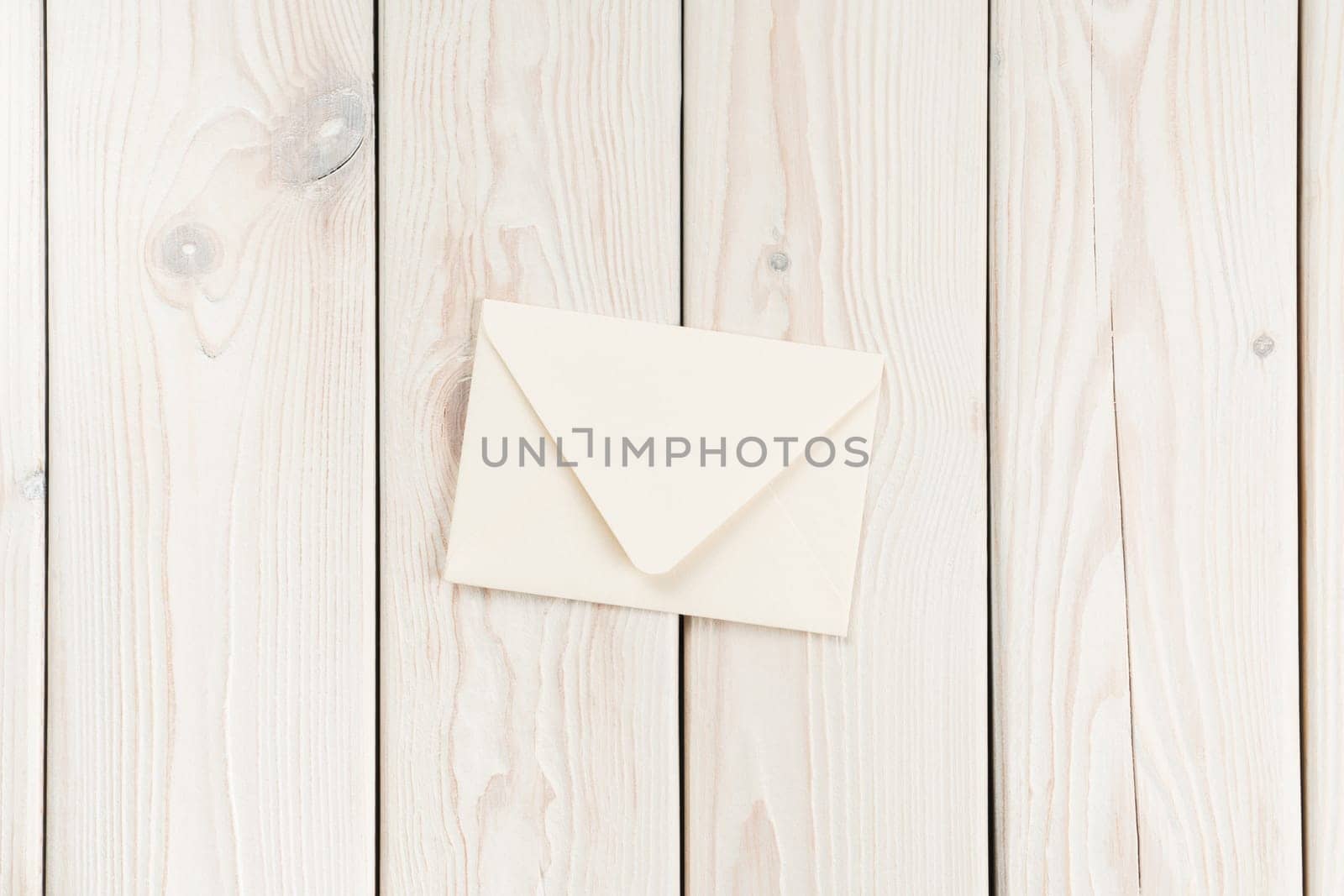White craft handmade closed paper envelope laying on white wooden plank background. Post card message, letter sending. New delivery and retro traditional invitation. Copy space, mockup, flat lay