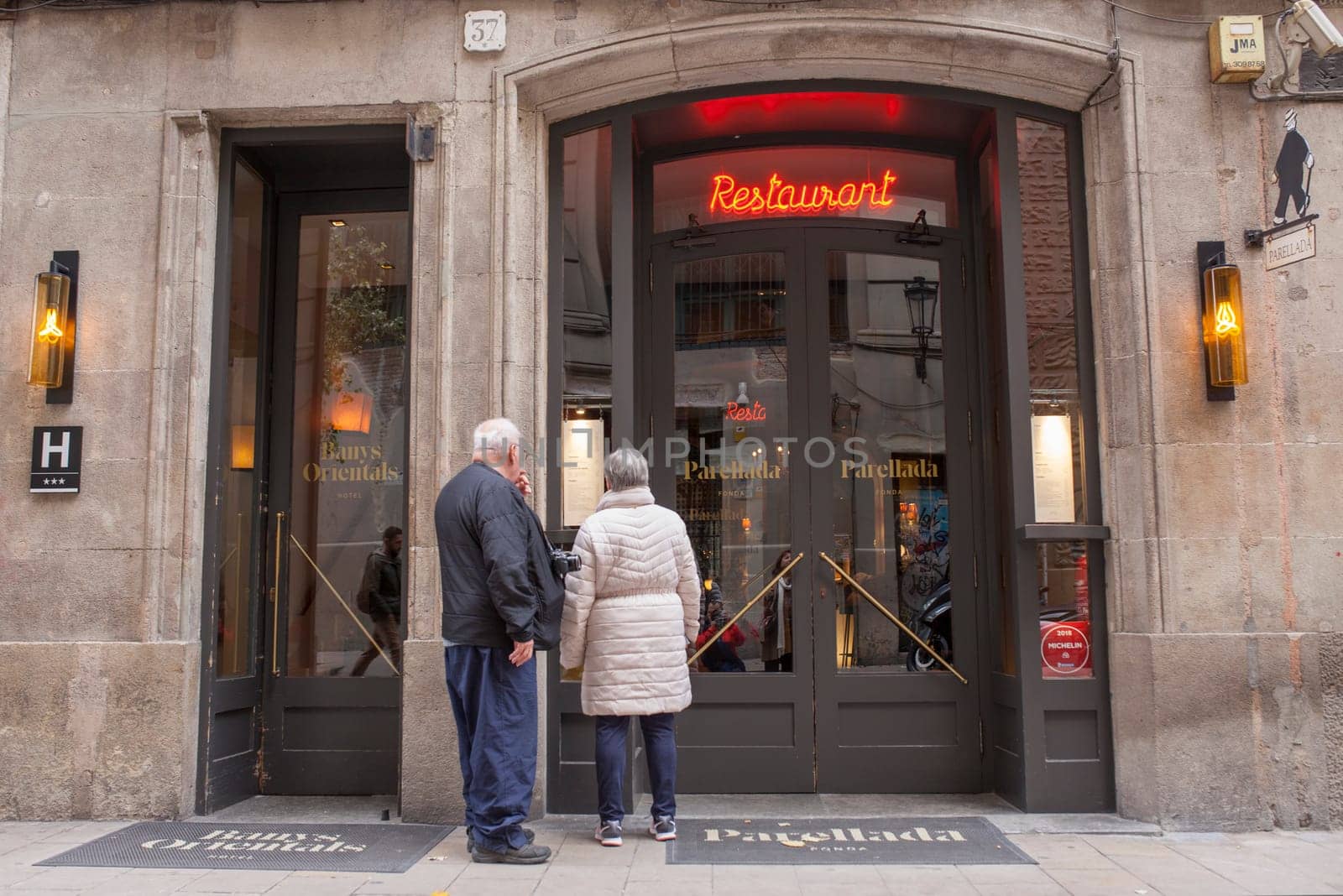 Barcelona, Spain - Dec 29th 2019: Elderly couple of tourists reading Parellada restaurant menu. Gothic Quarter, Catalonia, Spain