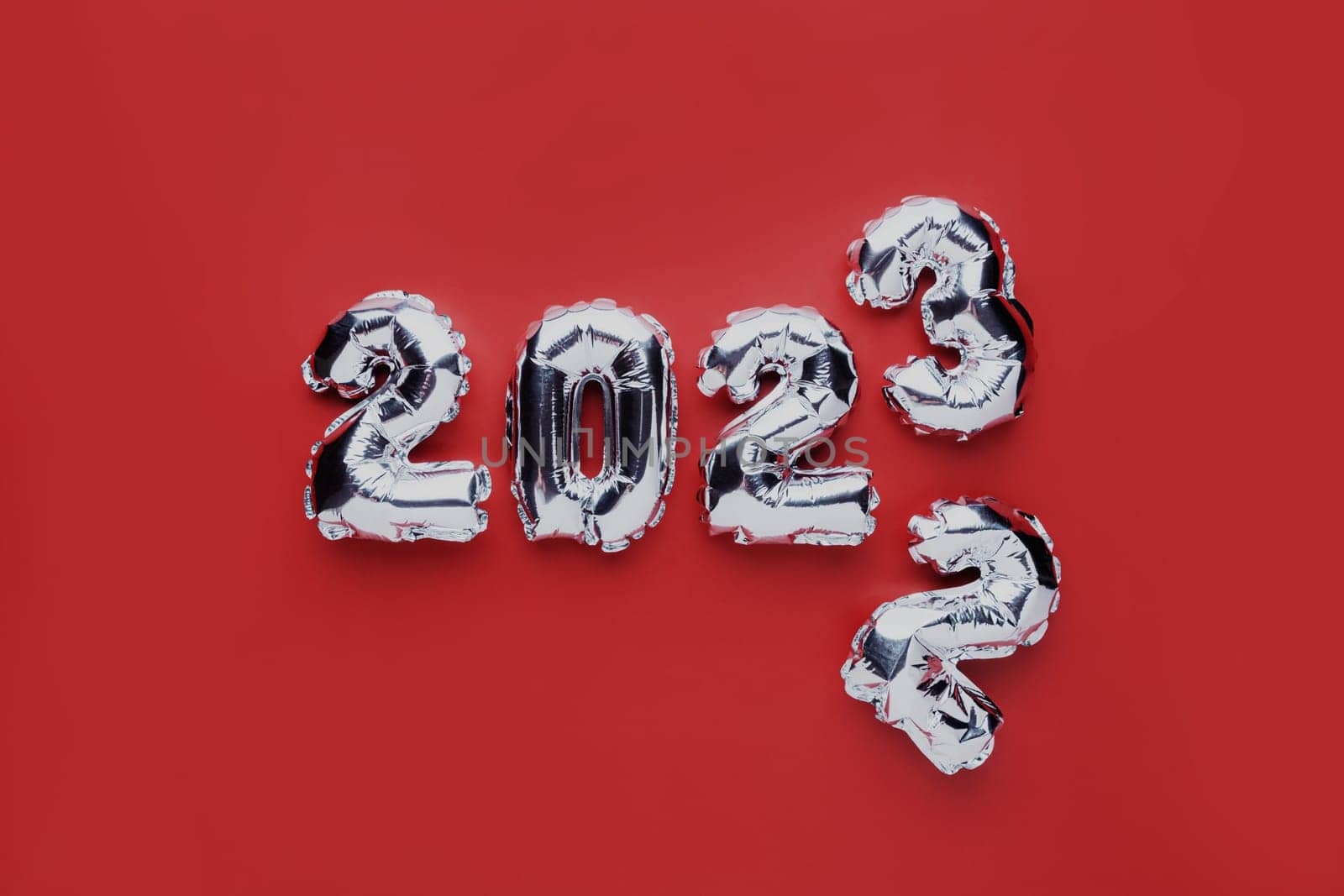 Christmas or New Year background. Red color flat lay with silver shiny 2023 balloon numbers in the center. Simple minimalistic greeting card.