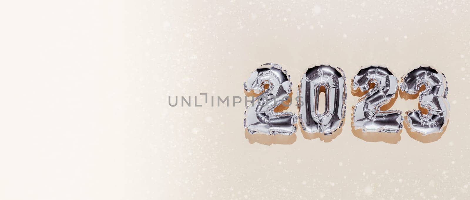 Christmas or New Year banner. Beige color flat lay background with silver shiny 2023 balloon numbers from right side. Copy space from left. White snow or sand decor. Simple minimalistic greeting card