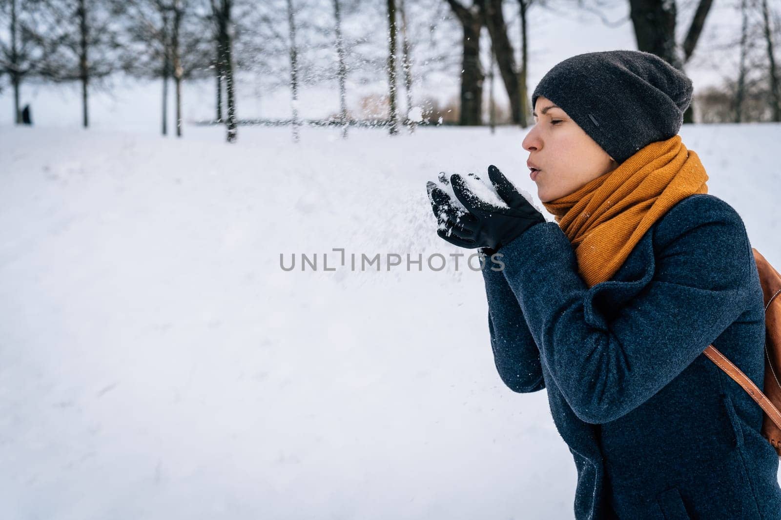 A young woman blows on the snow in her palms.