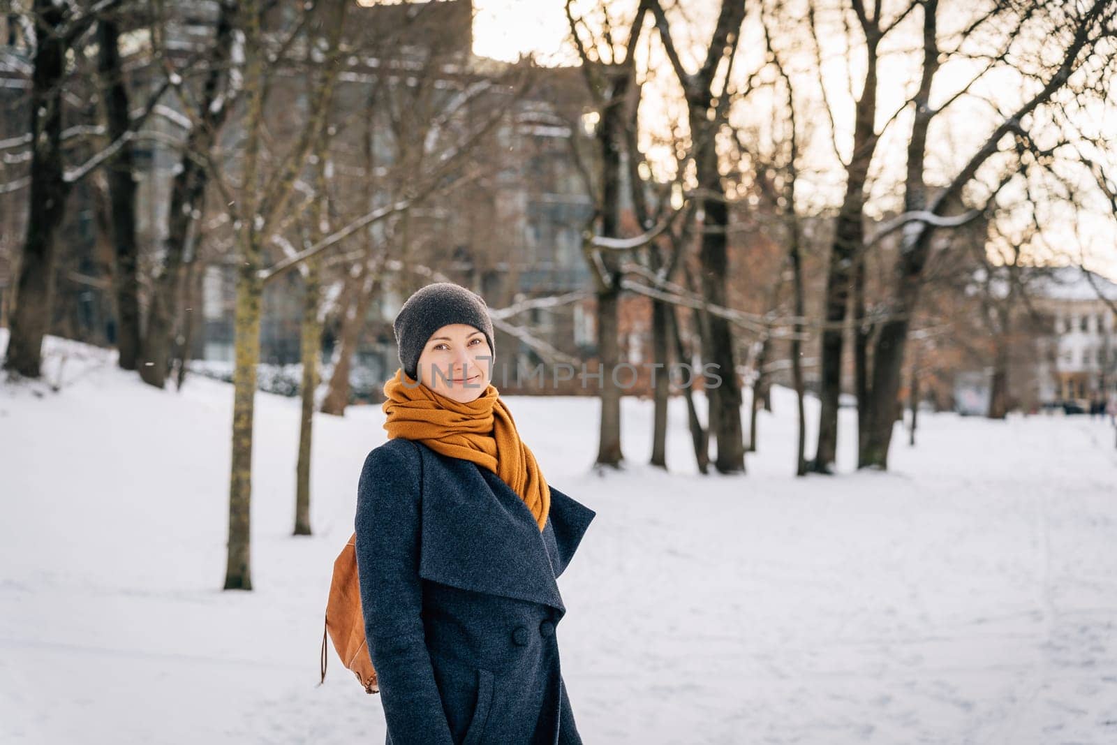 A woman in warm winter clothes looks into the camera and smiles in winter.