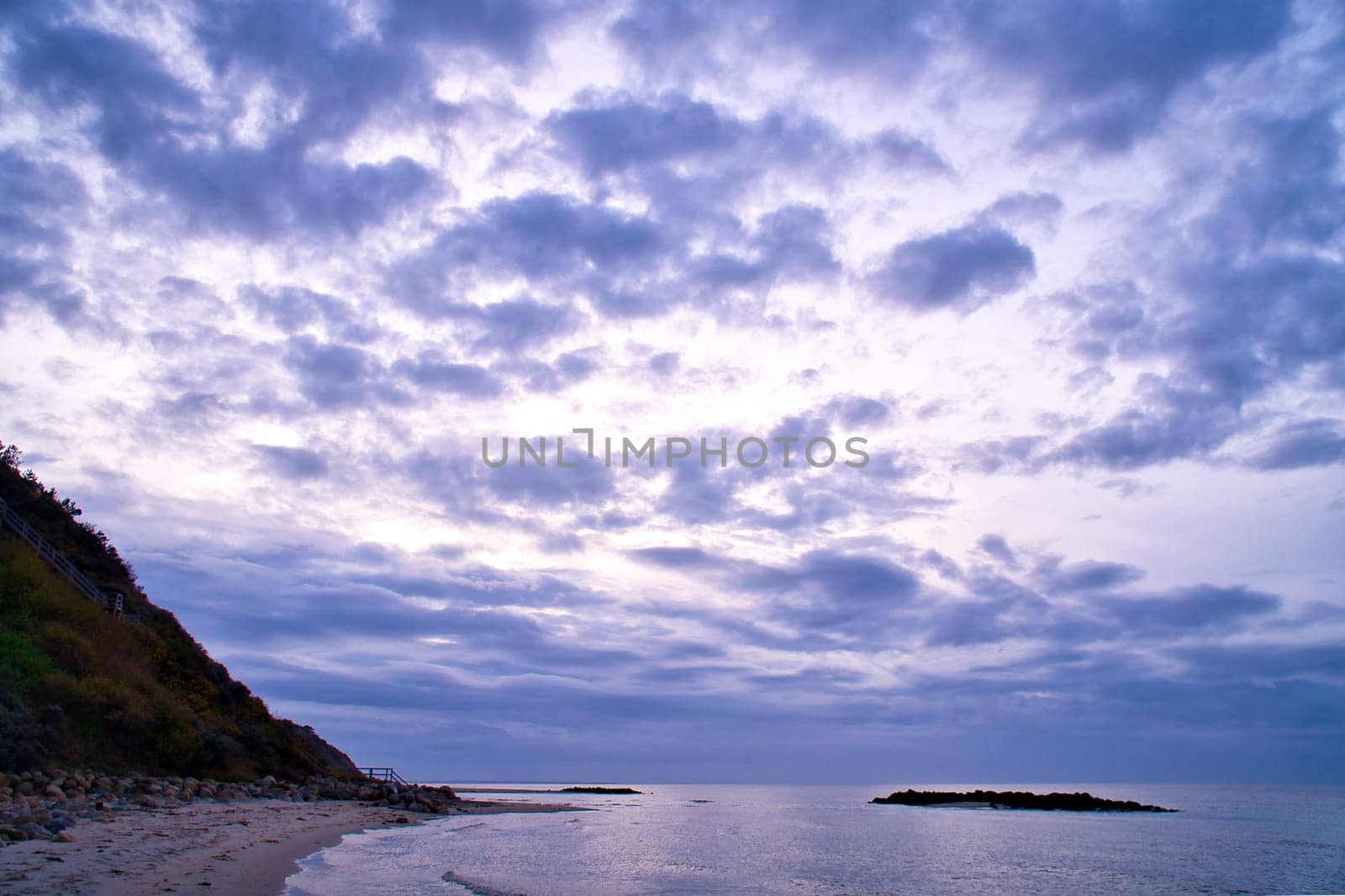 Sunset on the Danish coast. Beach, waves. Hill with trees in background. Landscape photo from sea