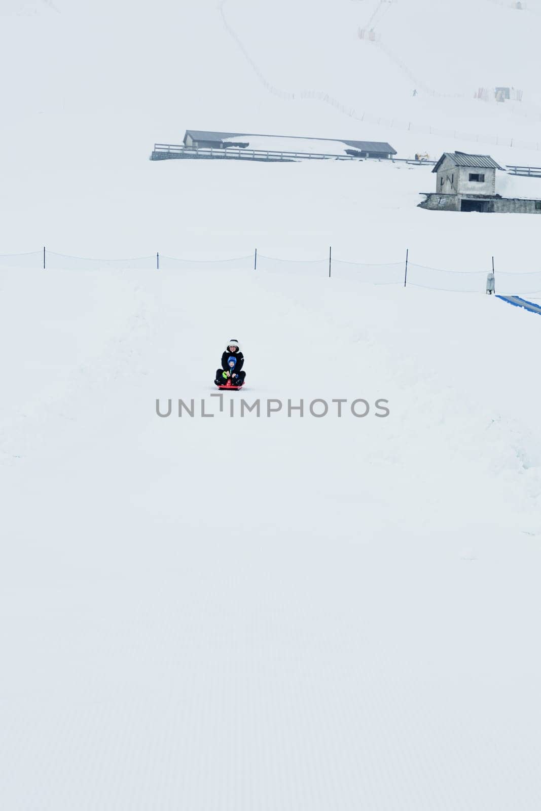 Mom and baby enjoy a sleigh ride. Sledding for children. Child riding a sleigh. Children play outdoors in the snow. Outdoor fun for family Christmas holidays.