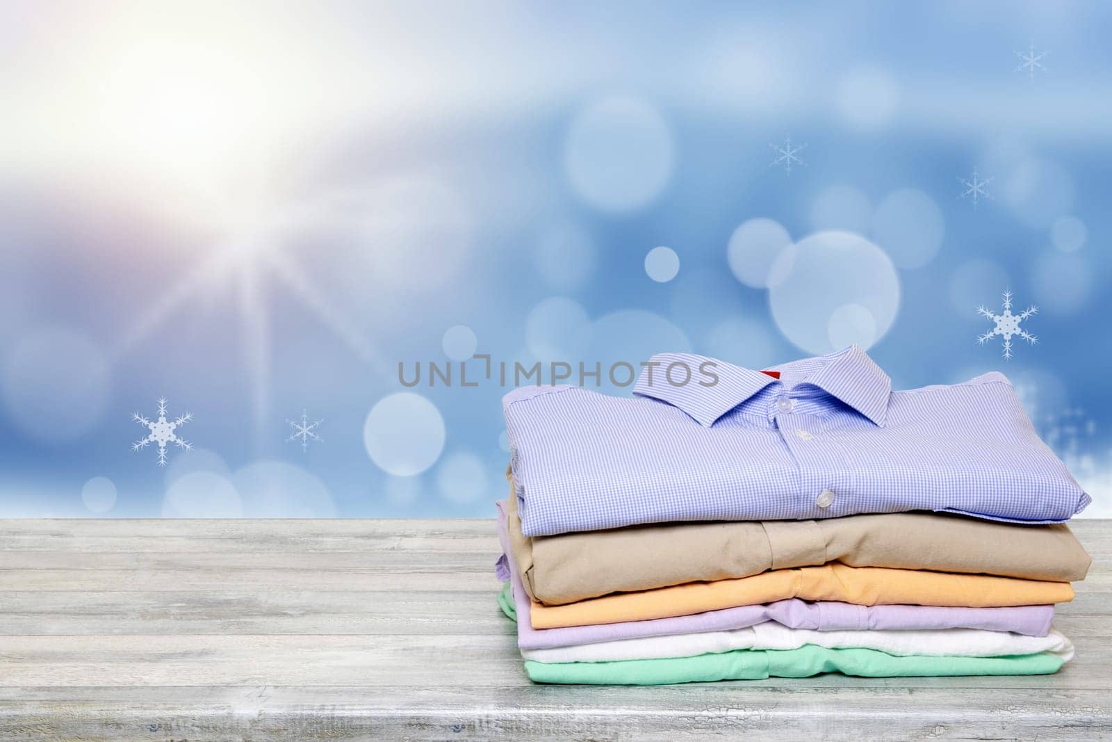 Stack colorful clothes. Pile of folded cotton shirts on a bright table with space for your display product montage over festive abstract blurred light christmas background.