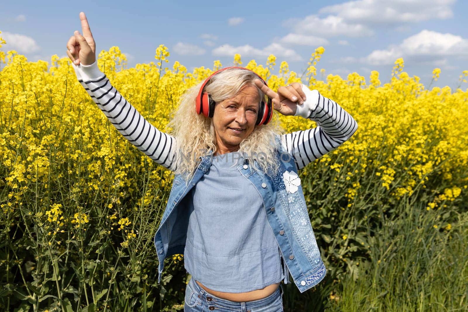 Elderly Woman listen to music with headphones in blooming canola field