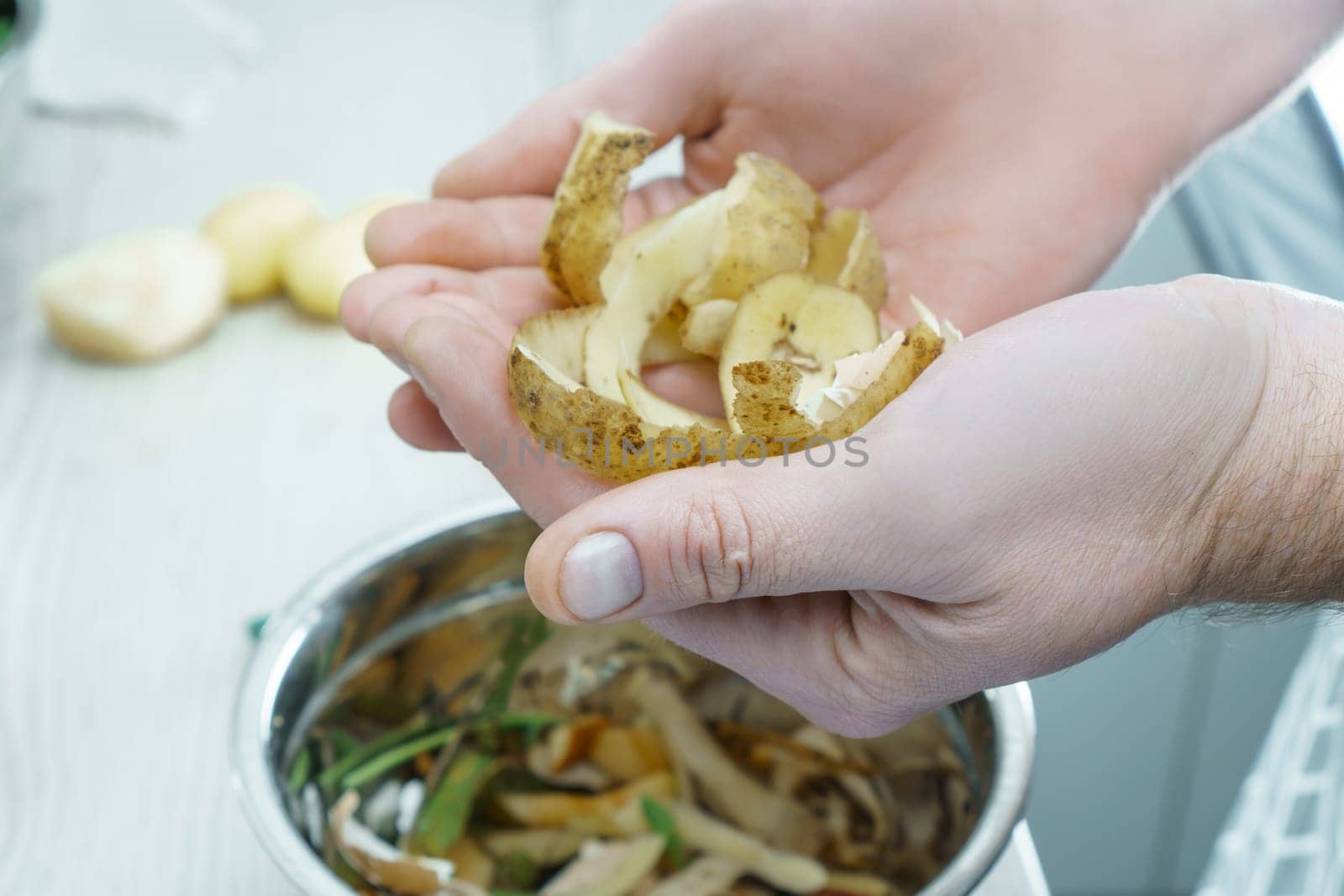 Male hands holding potato peels over bowl of vegetable peelings closeup. Cook on kitchen table, prepare ingredients, food scrap. Healthy nutrition, vegetables. Separate waste collection, waste free.