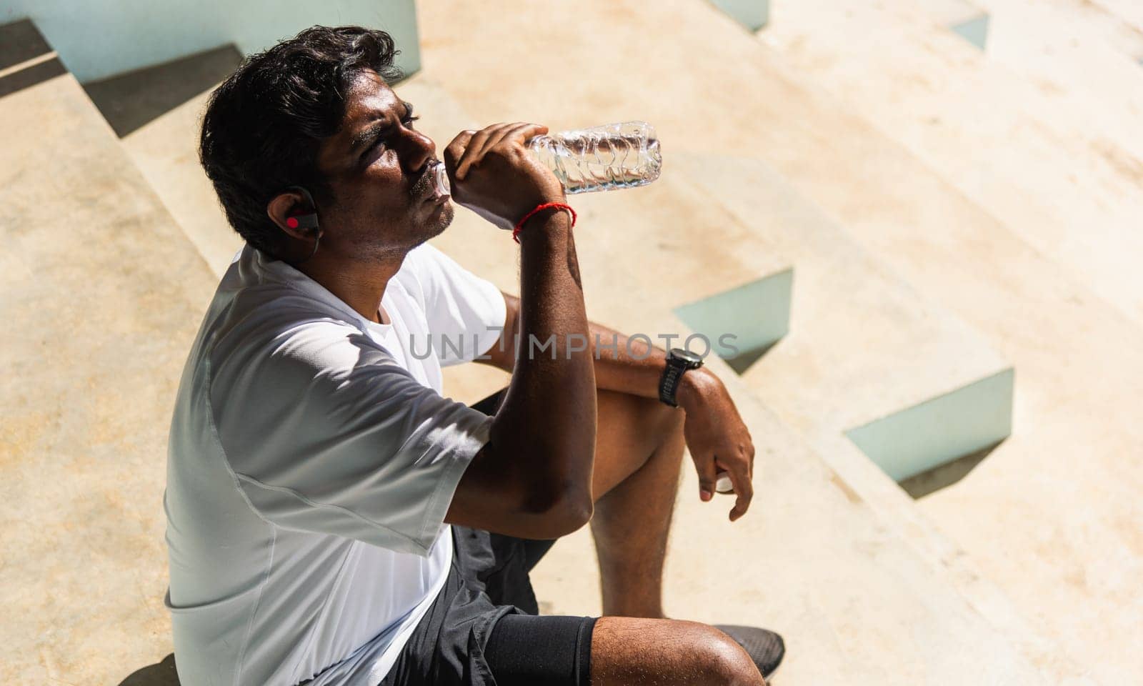 Close up Asian young sport runner black man wear athlete headphones he drinking water from a bottle after running at the outdoor street health park, healthy exercise workout concept