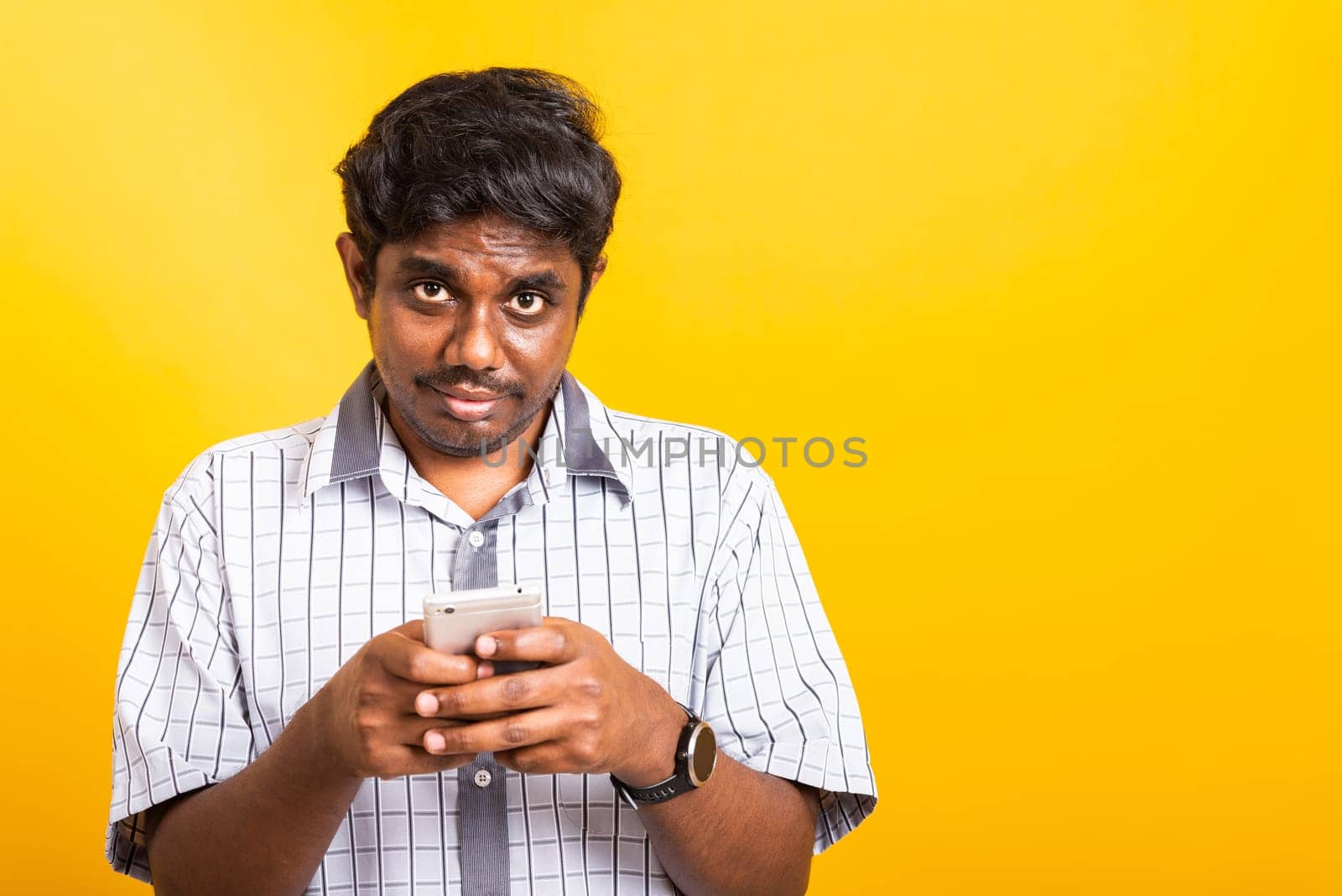 Asian happy portrait young black man smile standing wear shirt making typing or reading social message on mobile smart phone blank screen isolated, studio shot yellow background with copy space