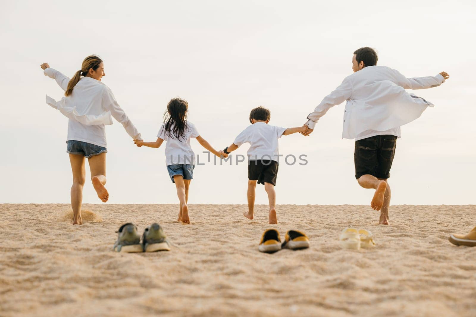 Happy family day. Back view of Asian having family parents with child fun holding hands together running to beach, lifestyle father, mother and kids relax take off shoes run on sand, holiday travel