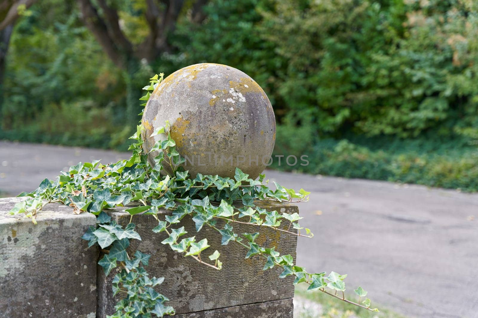 column with ball overgrown with ivy as decoration on a path in a public park