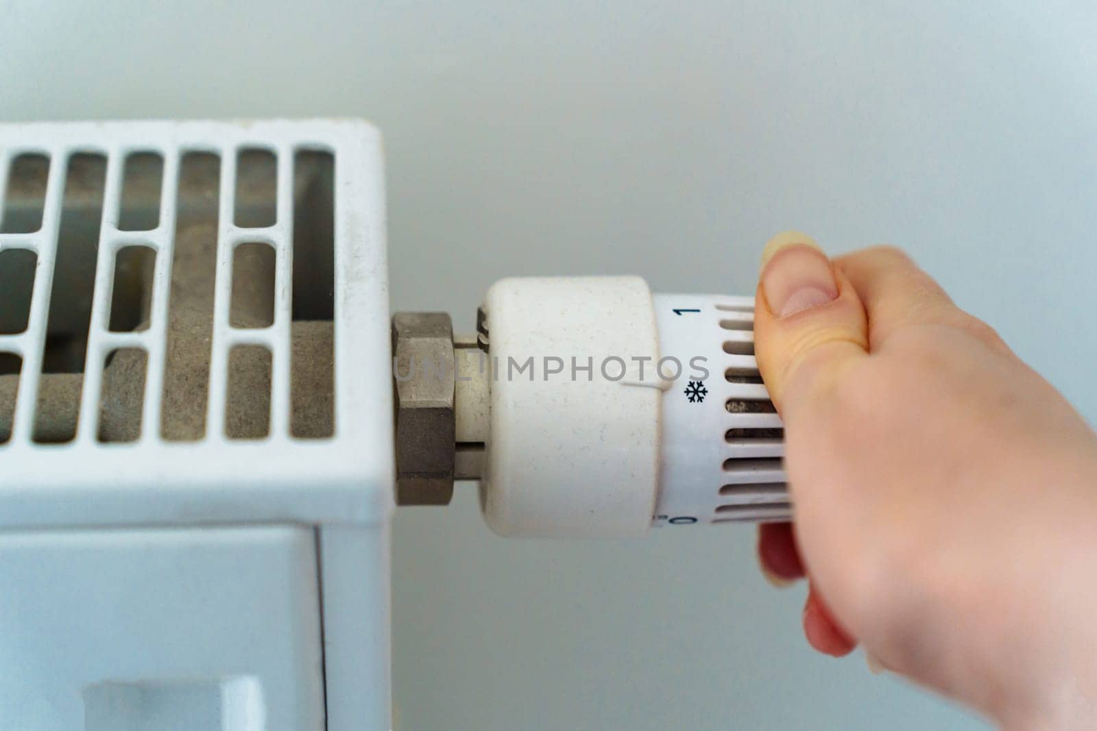 female hand completely turns off the heating radiator in apartment due to the rising cost of heating and utilities because of the energy crisis.