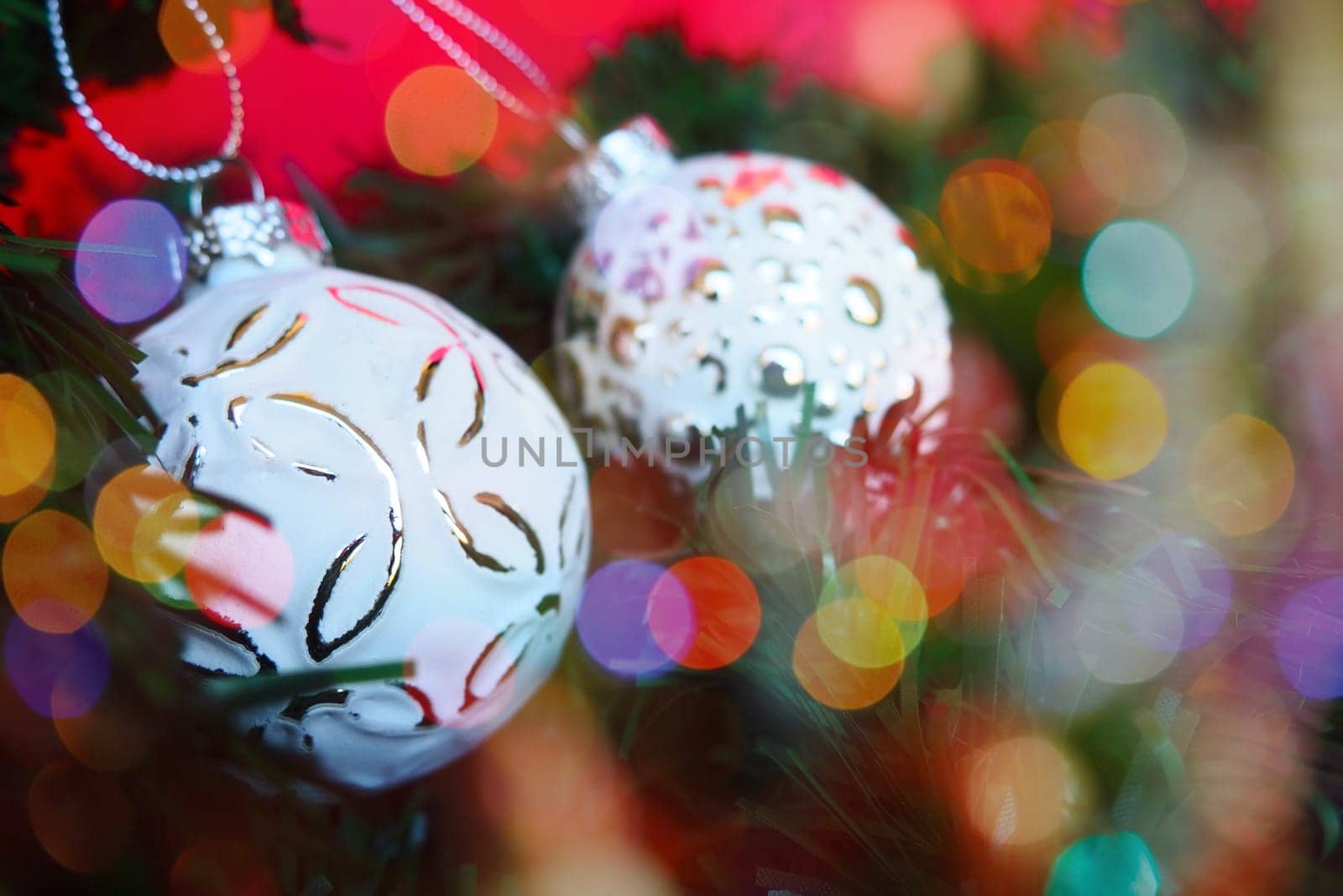 White trendy Christmas balls with sprinkles and a pattern on Christmas tree branches. Multicolored beautiful bokeh around the decorations. Postcard or New Year's Christmas background. Festive mood.