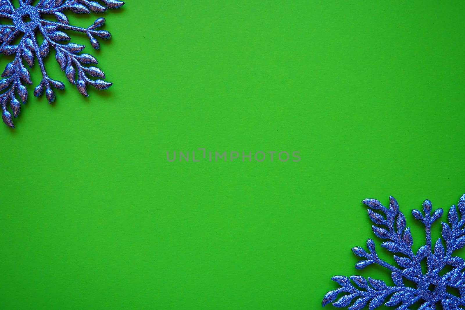 Christmas background with snowflakes. On a green background, two silver-blue snowflakes with sparkles are laid out. Happy New Year. Merry Christmas. Postcard or invitation. Copy space. Flat lay