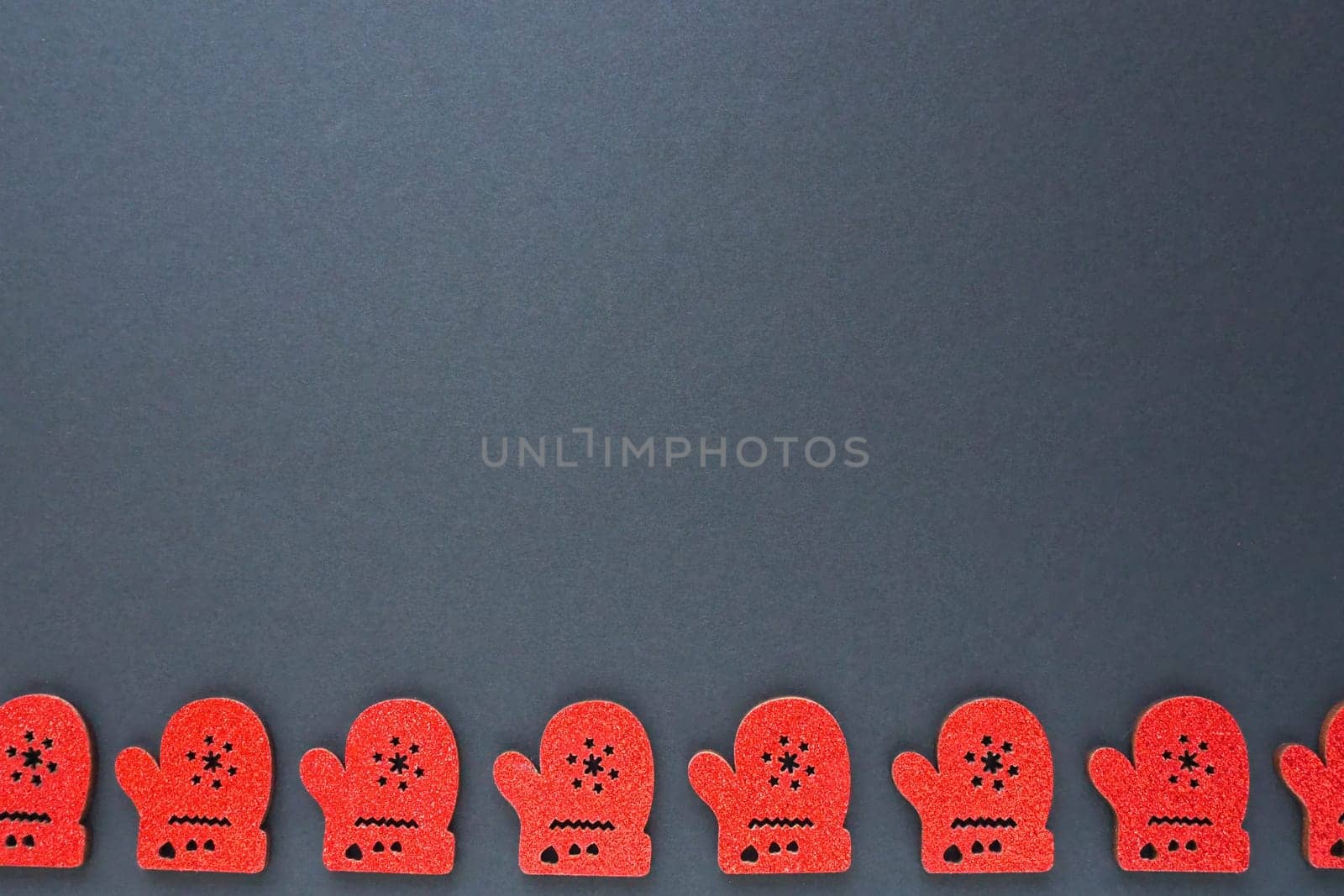 New Year and Christmas decorations in the form of red cardboard mittens with sparkles. The mittens are lined up along the bottom edge of the black paper. Christmas background. Copy space.